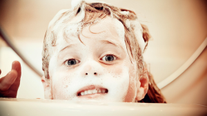 Child in a bathtub with soapy, sudsy hair being washed