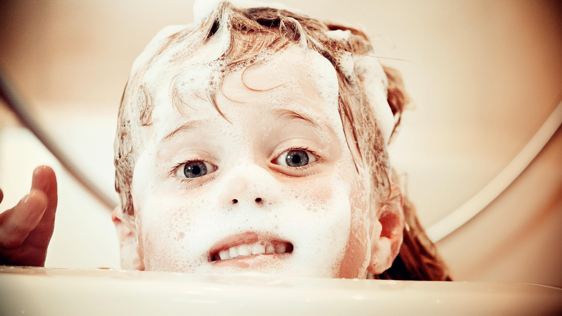 Child in a bathtub with soapy, sudsy hair being washed