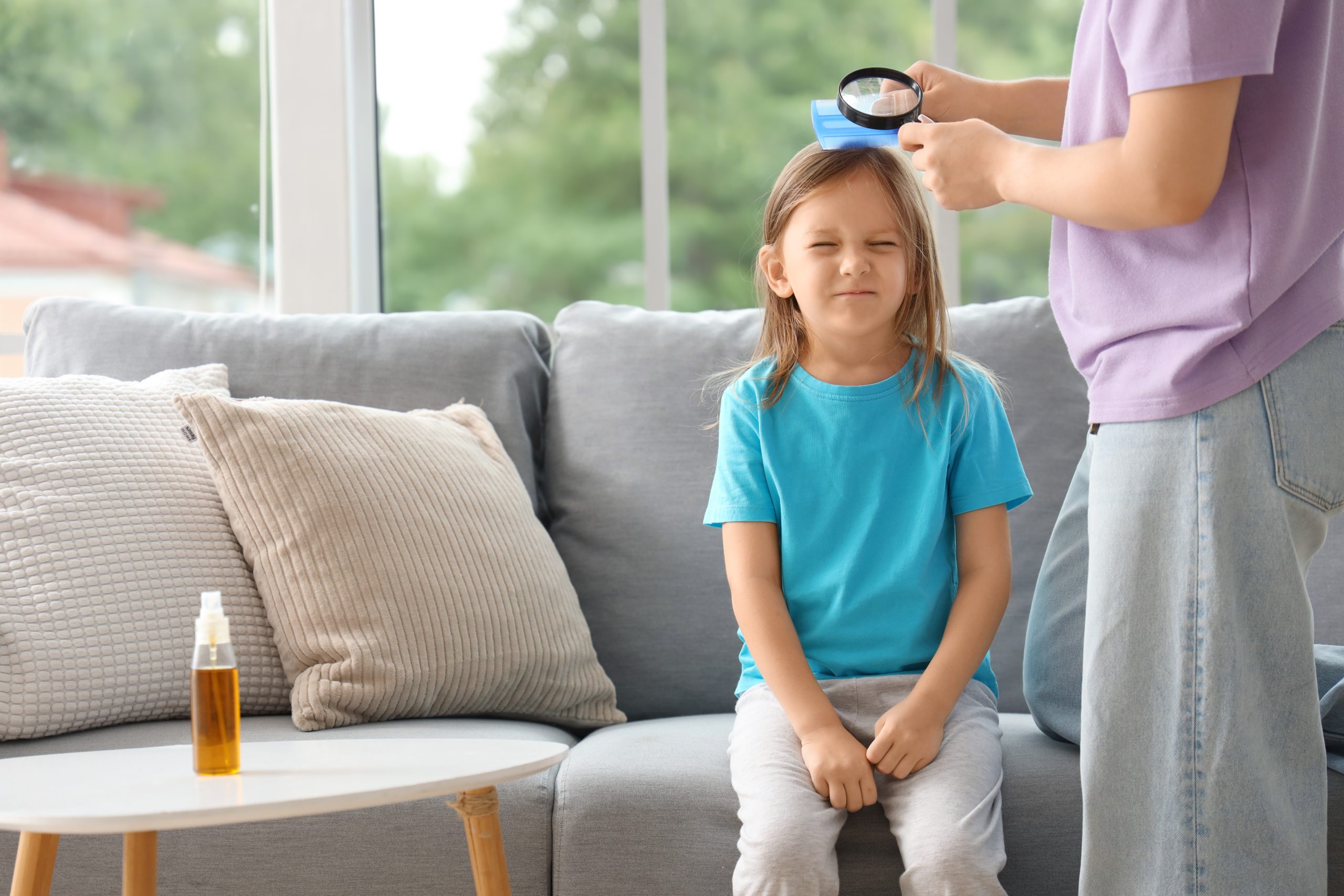 Parent gently combing through a child's hair section by section with a metal nit comb and a small magnifier during an at-home head check.