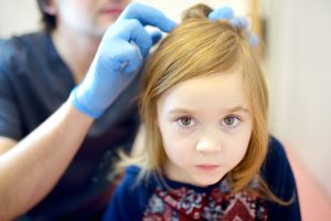 Clinician methodically parts and examines a child's scalp section by section under bright lighting, illustrating the careful identification step that catches newly hatched baby lice (nymphs) that quick bathroom-mirror checks miss.