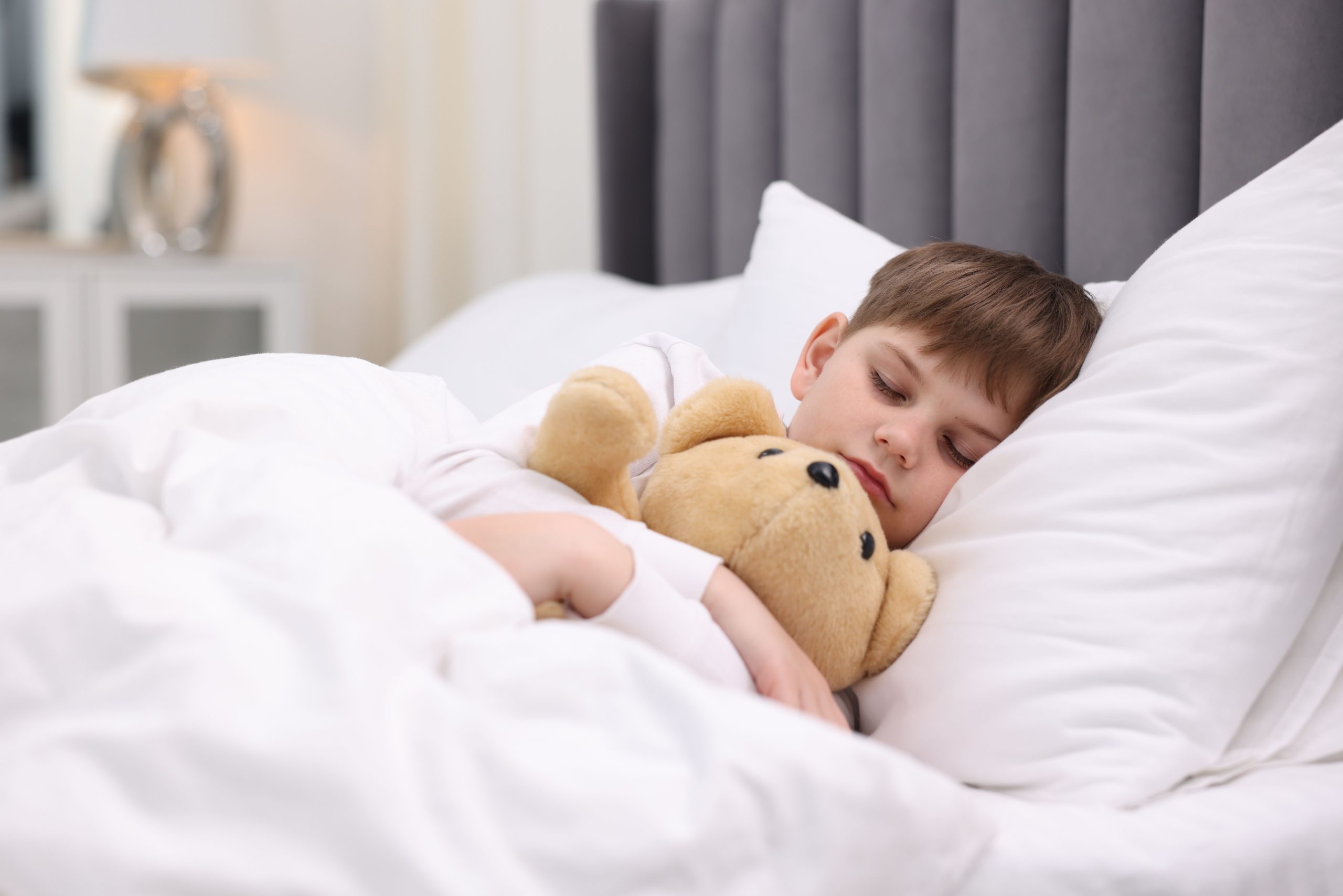 Cute little boy sleeping with his teddy bear on bed at home
