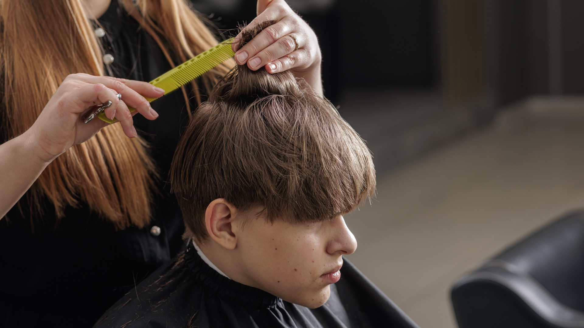 A young child getting a back-to-school haircut in a clean barbershop chair with a fresh cape and a stylist trimming their hair, illustrating the low-risk salon setting the article says rarely spreads head lice.