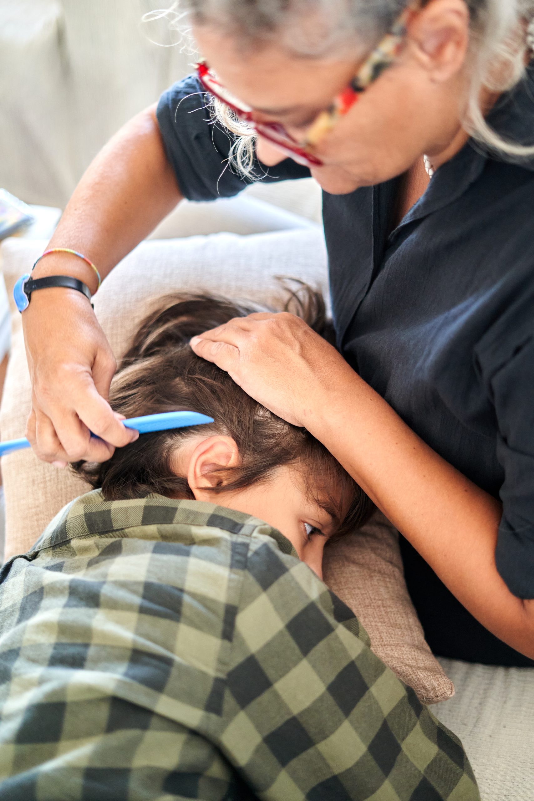 Woman Combs Child's Hair Gently on a Sofa