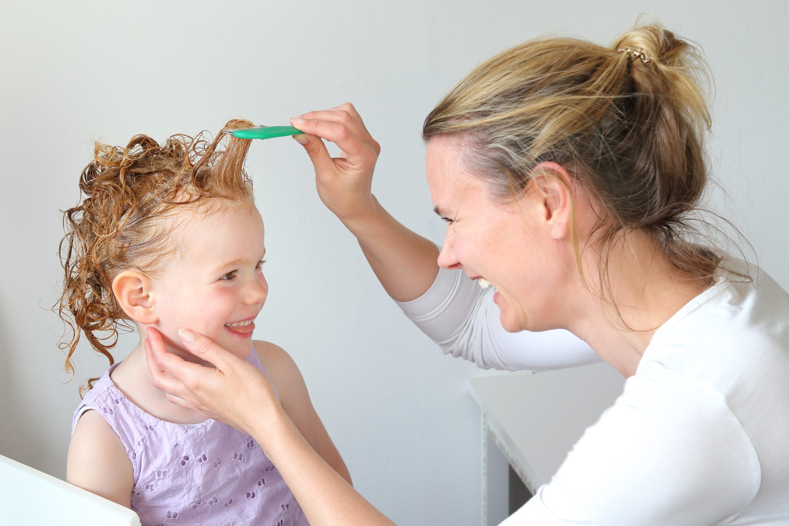 Mutter kämmt mit Läuasekamm Haare der Tochter