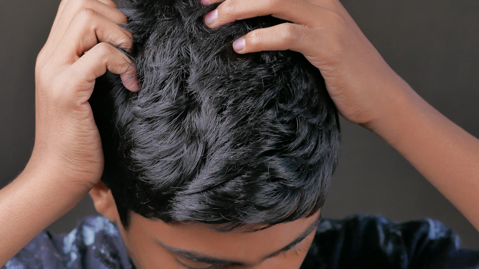 Person with short dark hair pressing both hands into their scalp.